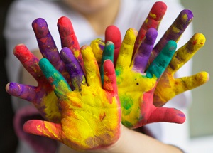 Child and adult's hands covered in colorful paint