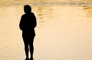 A woman stands silhouetted in front of rippling water.