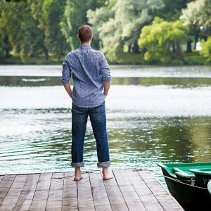 A man is looks out over a lake in a meditative moment.