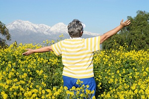 Older woman stands with amrs outstretched in field of wild flowers