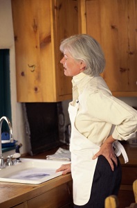 A woman stands at kitchen sink in obvious back pain. 