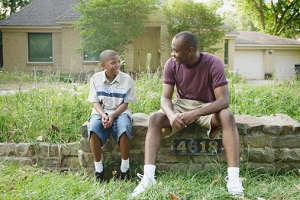 A man and his son sit together outside of a house.