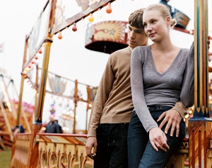 A couple leands together at an amusement park. 