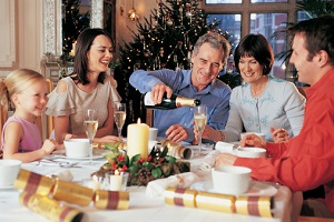 A man, surrounded by family, pours champagne at a holiday dinner.