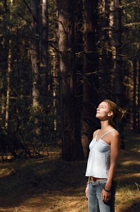 A young woman in woods looks up.