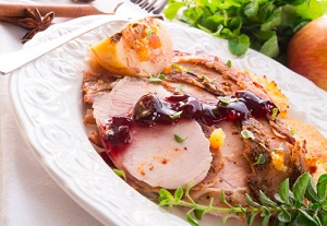 Cranberry sauce streaks slices of roasted turkey on a plate.