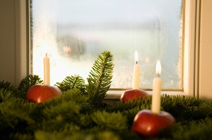 Holiday decorations sit on a windowsill, including apple candle-holders, candles, and pine cuttings