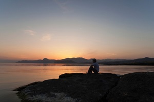 A man sits on rocks near water. 