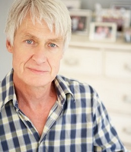 A sad older man stands in front of a dress full of family pictures.
