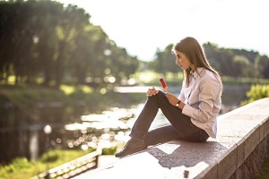 A young woman holding a popsicle sits by water.
