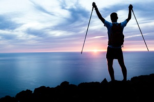 A man stops his hiking to look at the sun setting over the ocean. 