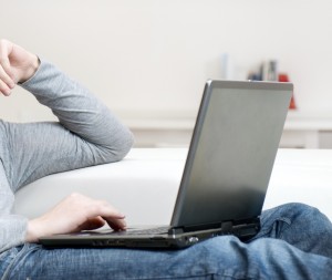 A man sits on a couch with a laptop on his lap.