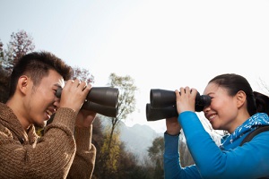 Young Asian couple in a forest smiling and  looking at each other through binoculars