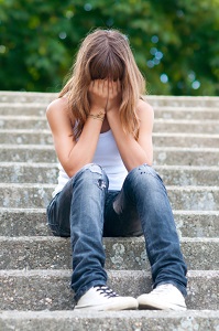 A girl sits on cement stairs covering her face.