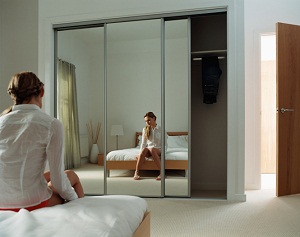 Woman is reflected in mirror while sitting on her bed thinking