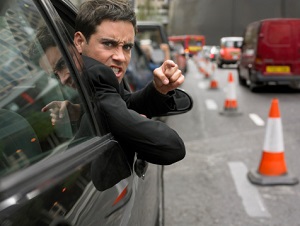 An angry man leans out of his car window and points his finger at someone.