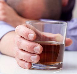 A man clasping a glass of liquor rests his head on his arm