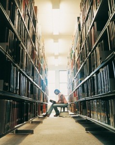 Woman sits between two rows of shelves in library reading