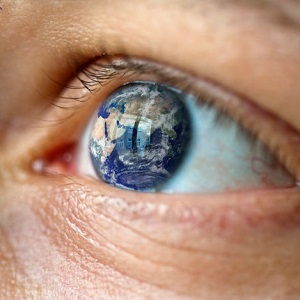 A close-up of a man's eye shows the earth reflected in it.