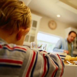 A boy sits at a kitchen table, looking sad, as his father scowls at him.