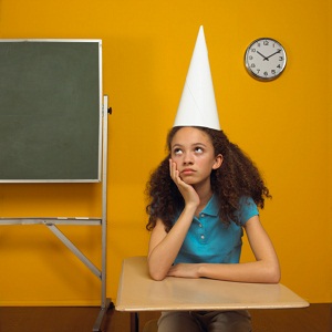 Girl with dunce cap sits in classroom