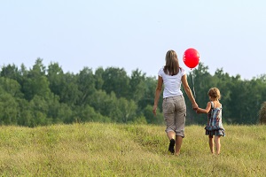 Mother and daughter walking in field with red balloon