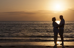 ET par står overfor hverandre på en strand ved solnedgang.