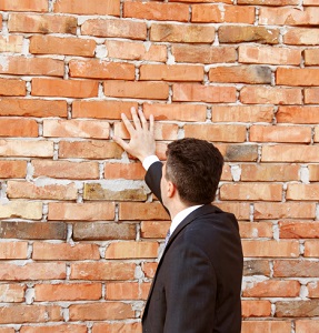 Man in a suit touching a brick wall