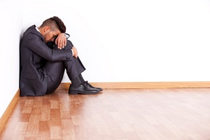 Man hugging knees in corner