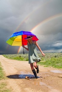 Woman skips with rainbow umbrella while strom crosses the sky