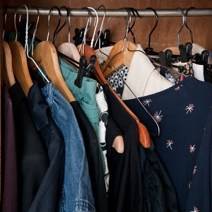 Clothing on hangers are packed tightly in a closet.