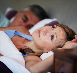 Distressed woman lies next to sleeping man
