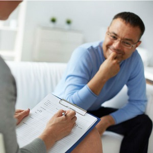 A man looks thoughtful as a therapist asks him questions off her clipboard.