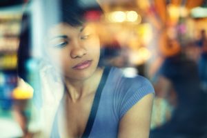 View through window of woman sitting, lost in thought