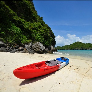 A kayak is sitting on a sandy beach, a few yards away from the water.