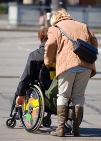 A woman pushes her husband in a wheel-chair.