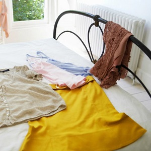The bottom end of a bed is shown with clothes laying on it.
