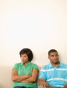 Couple sitting in front of white wall, arms crossed, looking away from each other as if frustrated