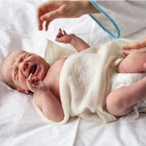 A new born baby cries as its mother's hands reach to comfort the infant.