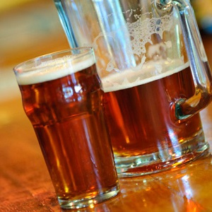 A glass of beer and a half-empty pitcher sit next to each other on a bar.