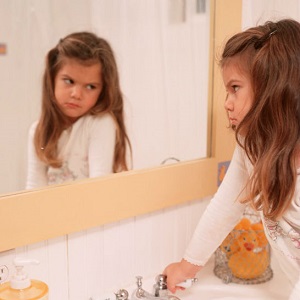 A young girl looks disapprovingly at herself in the mirror.