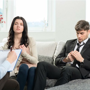A couple sits with a therapist as the man looks uninterested.