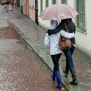 Two women walk with their arms around each other while sharing an umbrella.