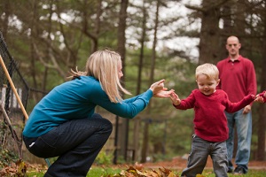 Parents help their infant walk in a forested setting