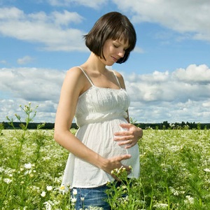 A pregnant woman stands in a field of flowers, holding her belly and smiling.