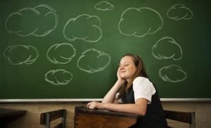 Student daydreaming with thought bubbles on chalkboard