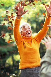 An older woman throws fall leaves in the air.