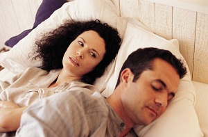 Unhappy woman and sleeping man lying in bed