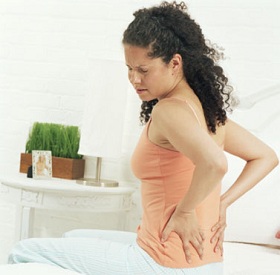 Woman sitting on bed holding back in pain