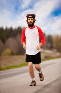 Young man with long hair, beard, and headband running down country road in red and white tee shirt, breathing heavily